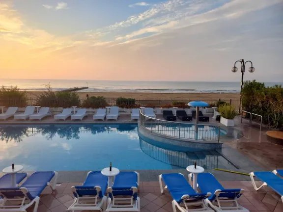 Bazén hotelu Elpiro v Lido di Jesolo v Itálii při západu slunce s výhledem na písečnou pláž a Jaderské moře.