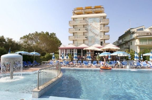 Venkovní bazén hotelu Elpiro v Lido di Jesolo v Itálii s lehátky a budovou hotelu v pozadí, ideální pro dovolenou u moře.