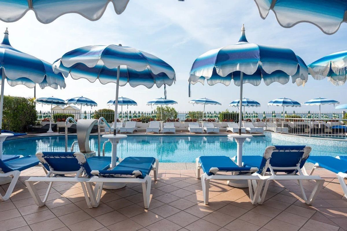 Venkovní bazén hotelu Elpiro v Lido di Jesolo v Itálii s lehátky a slunečníky, hotel přímo u pláže s výhledem na moře.