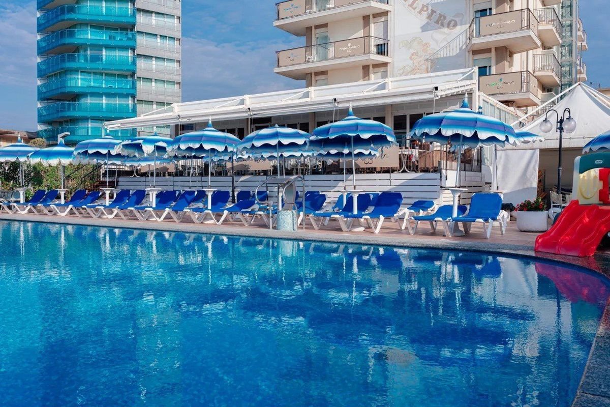 Venkovní bazén hotelu Elpiro v Lido di Jesolo v Itálii s lehátky a slunečníky, hotel u pláže ideální pro letní dovolenou.