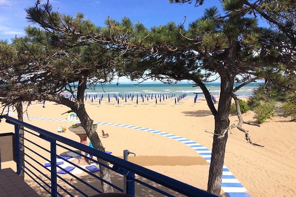 Písečná pláž v Lignano Riviera v Itálii s řadami slunečníků a výhledem na Jaderské moře, ideální pro letní dovolenou u moře.