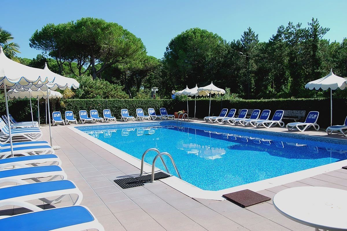 Venkovní bazén hotelu Old River v Lignano Riviera v Itálii s lehátky a slunečníky, ideální místo pro relaxaci během dovolené u moře.