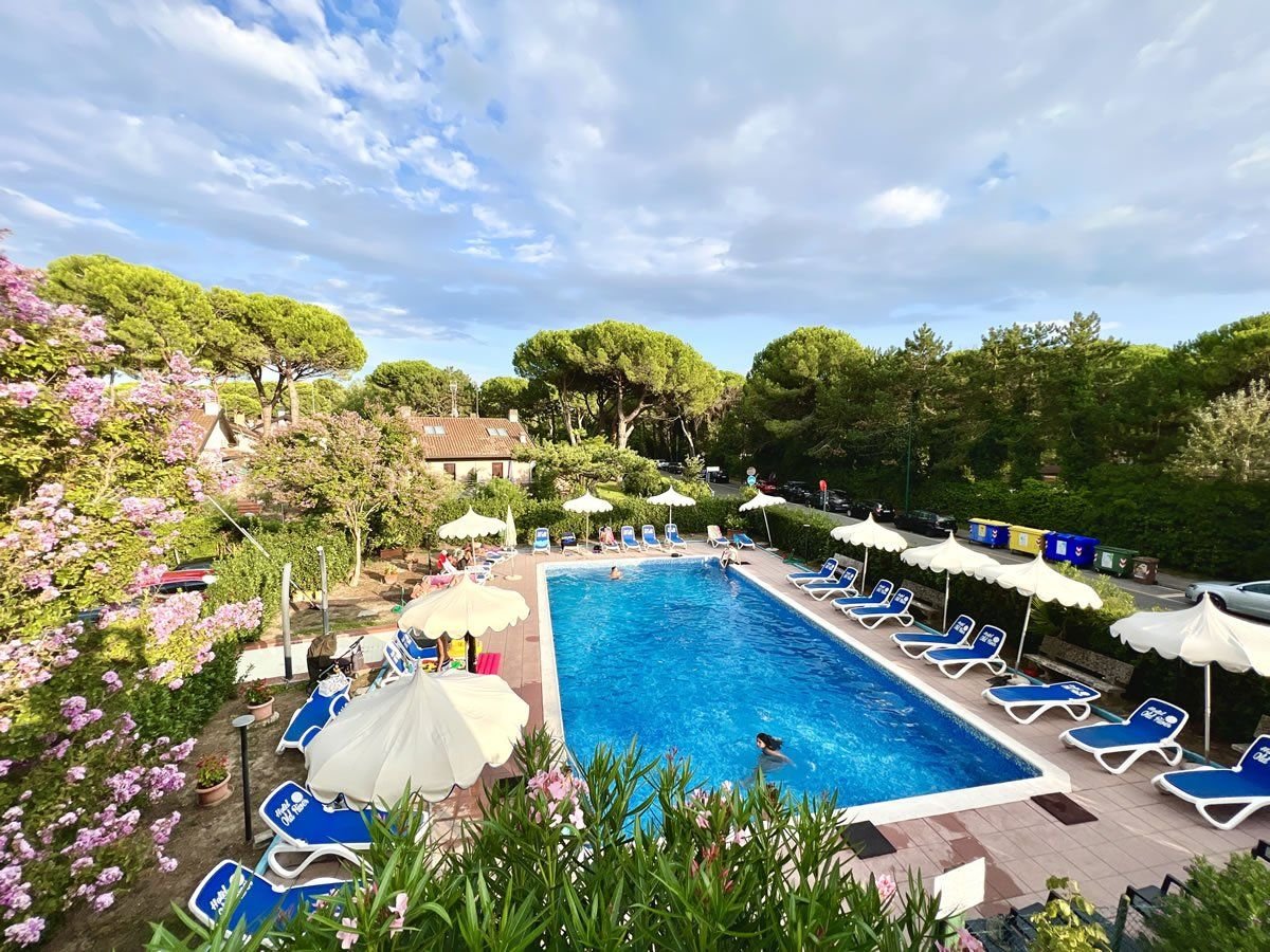 Venkovní bazén hotelu Old River v Lignano Riviera v Itálii obklopený lehátky, slunečníky a středomořskou zelení, ideální pro rodinnou dovolenou u moře.