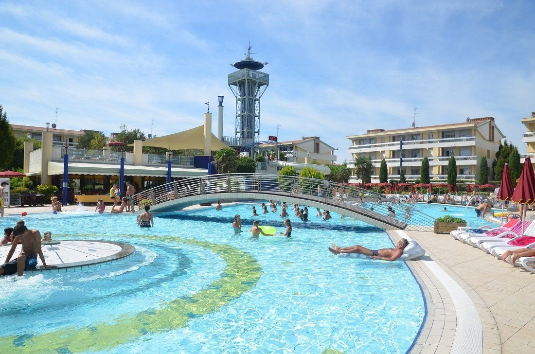 Hlavní bazén s mostkem ve Villaggio Planetarium Resort v Bibione v Itálii, oblíbený apartmánový resort pro rodinnou dovolenou u moře.