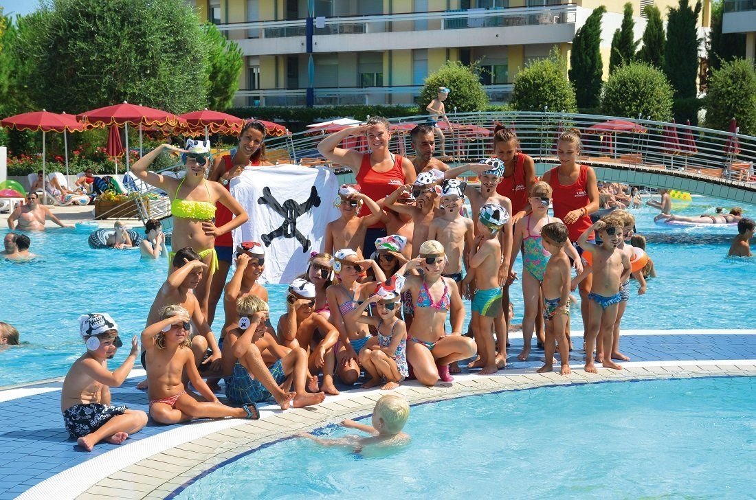 Děti s animátory u bazénu ve Villaggio Planetarium Resort v Bibione v Itálii, rodinný resort s animačním programem a bazénem.