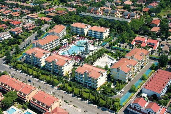 Letecký pohled na villaggio Planetarium Resort v Bibione v Itálii s venkovním bazénem a apartmánovými domy, ideální pro letní dovolenou u moře.
