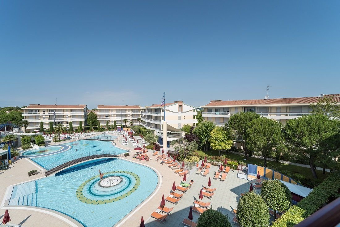 Bazénový komplex Villaggio Planetarium Resort v Bibione v Itálii s lehátky a apartmánovými domy, ideální pro rodinnou dovolenou u moře.