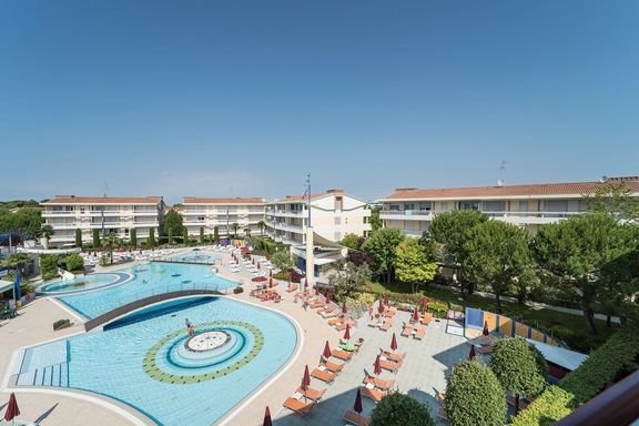 Bazénový komplex Villaggio Planetarium Resort v Bibione v Itálii s lehátky a apartmánovými domy, ideální pro rodinnou dovolenou u moře.